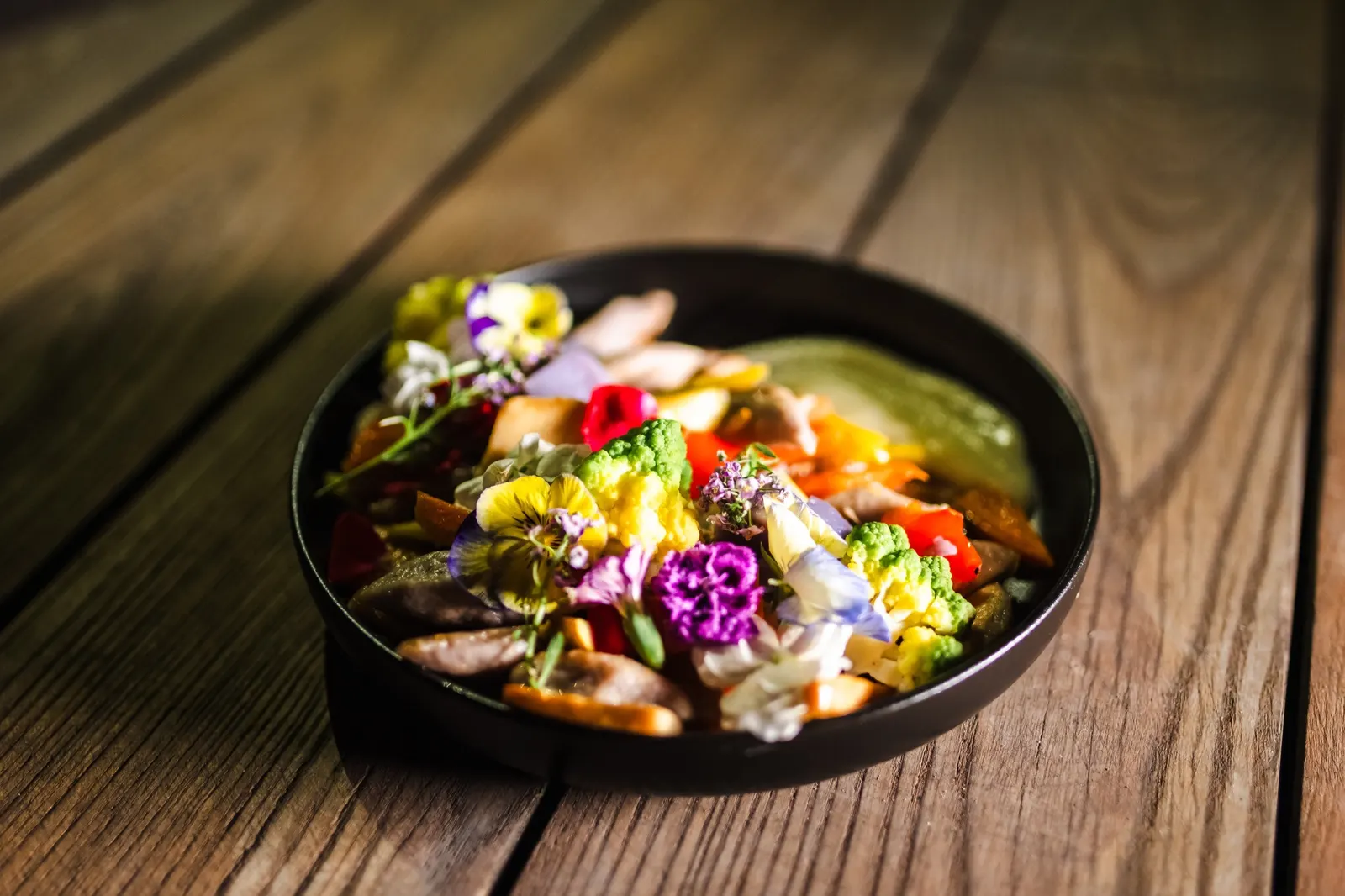 Bunter Salat mit Blüten in einer schwarzen Schale
