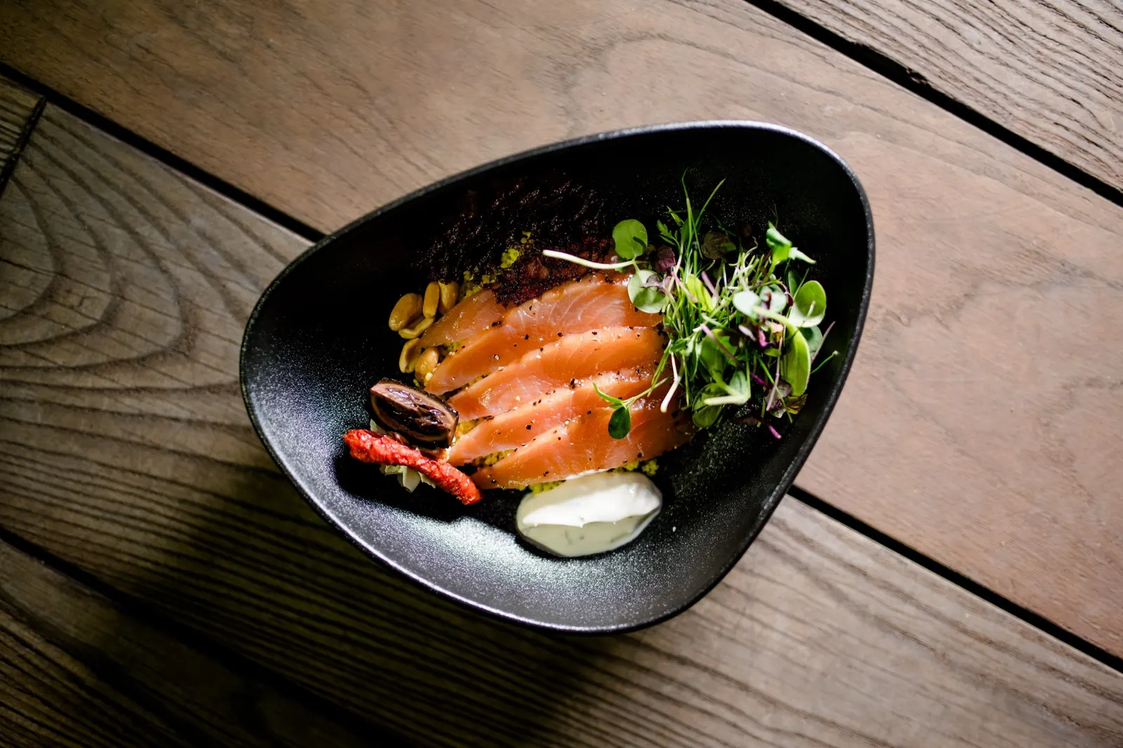 Lachs mit Salat in einer schwarzen Schale auf Holz