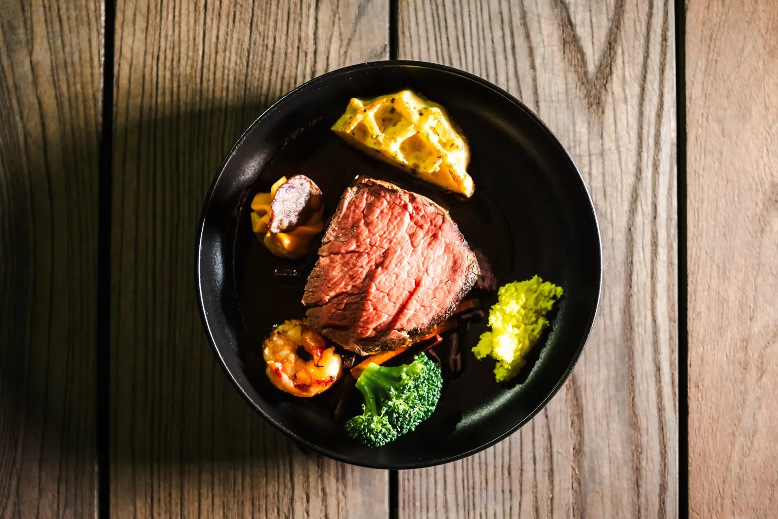 Rinderfilet mit Gemüse in einer schwarzen Schale auf Holz