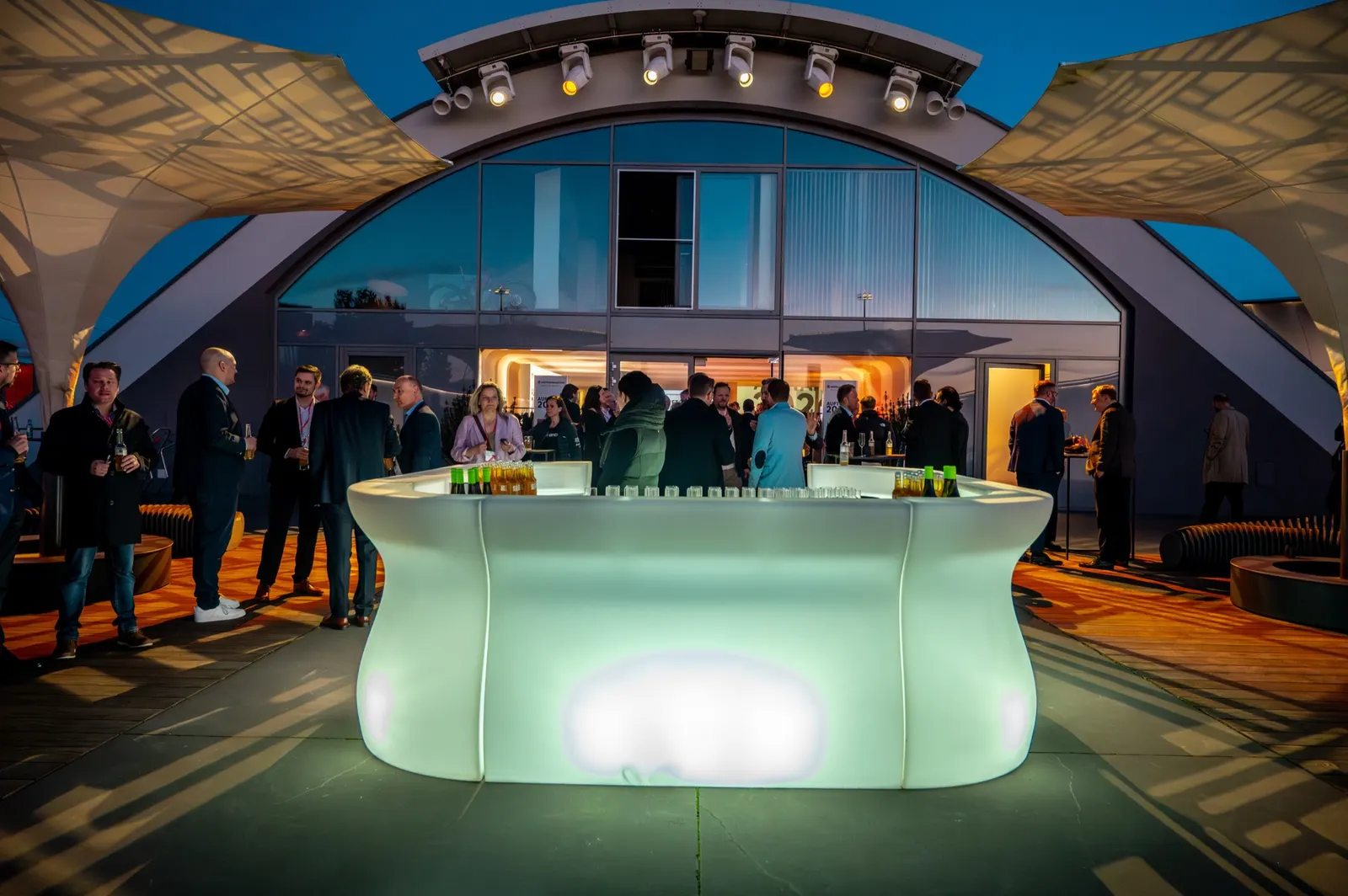 Leuchtende Bar auf der Terrasse vor dem beleuchteten Hangar am Abend